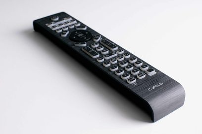 Télécommande iR14 Cyrus, vue en perspective, surface noire, nombreux boutons gris et noirs, logo en bas à droite