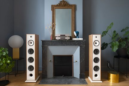 Heledast puidust nelja kõlariga hi-fi põrandakõlarite paar musta kamina mõlemal küljel modernses elutoas