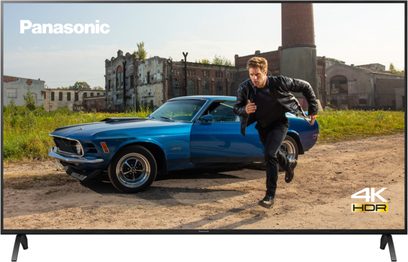 Modrý Ford Mustang z roku 1970 zaparkovaný před zchátralou průmyslovou budovou, muž stojící vedle otevřených dveří auta