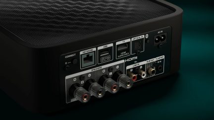 Bakside av en svart forsterker med HDMI-, USB-, nettverks-, optiske porter, høyttalerkontakter, strømforsyning