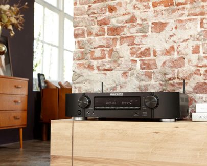 Černý stereofonní ampli-tuner Marantz umístěný na světlém dřevěném nábytku před zdí z červených cihel