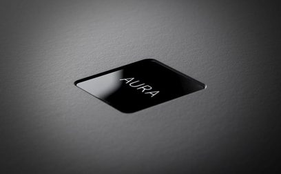 Передпідсилювач фонокоректора Rega Aura MC чорного кольору, вид зверху під кутом 45 градусів, глянцева поверхня, напис Aura білим кольором