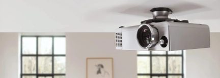 Vidéoprojecteur gris argenté fixé au plafond par un support noir, avec grand objectif à l’avant, vu de trois quarts