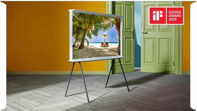 Samsung The Serif QE65LS01BB 2022 65" TV på fod, der viser et tropisk strandmiljø med palmer og parasoller