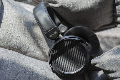 Hifiman HE400i 2020 Edition atvērtās hifi austiņas, melnas, novietotas uz gaiši pelēka auduma, redzamas no kreisās puses trīs ceturtdaļu skatu