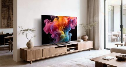 Móvel de TV baixo com aspeto de madeira clara, com portas e nichos abertos, por baixo de uma televisão de ecrã plano numa sala de estar luminosa