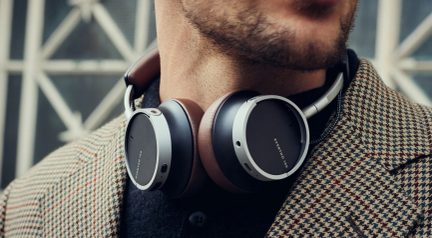 Mat siyah, gümüş renkli metal halkalı ve kahverengi deri yastıklı supra-aural kulaklık, bir kişinin boynunda, üç çeyrek yakın plan görünüm