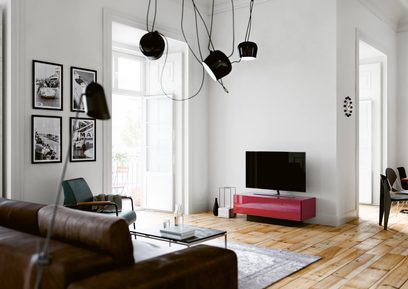 Moderní obývací pokoj s hnědou koženou pohovkou, červeno-černým televizním nábytkem, černými závěsnými lampami, světlými dřevěnými podlahami, bílými stěnami a zarámovanými fotografiemi