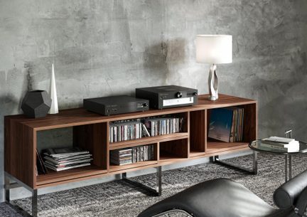 Mueble bajo de nogal con estanterías abiertas sobre patas metálicas, vista oblicua, dos aparatos negros, lámpara blanca, CDs y vinilos