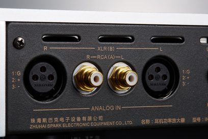 Primo piano frontale sui connettori XLR a tre poli neri e RCA dorati incassati in un pannello posteriore in metallo nero opaco con bordo in alluminio argento del preamplificatore per cuffie Cayin IHA-8 argento
