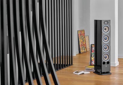 Schwarze Audiolautsprecherbox, abstraktes buntes Gemälde, Bücher, Parkettboden, weiße Wand mit vertikalen schwarzen Streifen