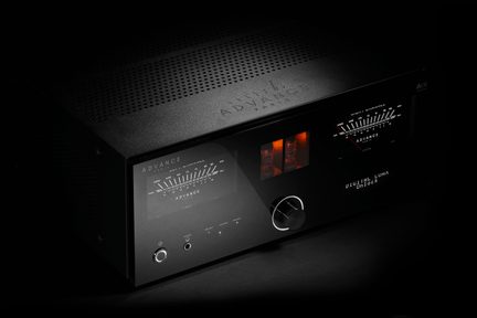 Černý kovový zesilovač, skleněný čelní panel s VU metry, zářivě oranžové elektronyky a velké tlačítko, pohled ze tří čtvrtin