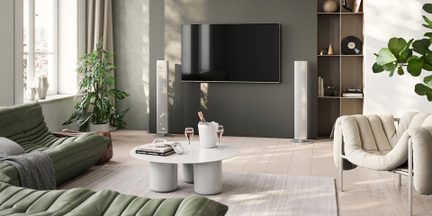 Moderne stue med modulopbygget grøn sofa, beige lænestol, hvidt sofabord, væghængt tv og hvide gulvhøjttalere