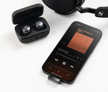 Черни безжични слушалки Sennheiser в отворена кутия до смартфон с музика и съответстващи слушалки върху глава