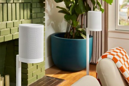 Hvid trådløs Sonos-højttaler monteret på stativ, installeret i en moderne stue nær en grøn pejs