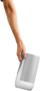 Bras et main tenant une enceinte sans fil portable blanche de forme cylindrique avec grille grise sur la partie supérieure