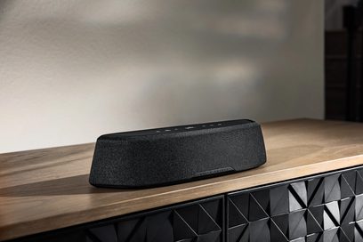 Sort rektangulær Polk Audio MagniFi Mini AX soundbar med maskeovertrukket overflade, placeret på en lys træhylde