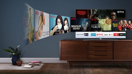 TV-en viser Netflix-grensesnittet med flere serier, plassert på et trehylle i en stue