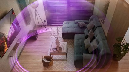 Surround-hjemmebiografsystem i moderne stue med stor grå hjørnesofa og vægmonteret TV, lilla lydbølger