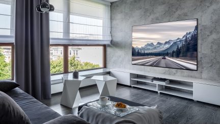 Moderne stue med grå sofa, geometrisk sofabord, TV og store vinduespartier med udsigt over et snedækket bjerglandskab