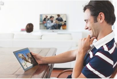 Smilende mand ser på et tv-skærmbillede, der viser et billede af en gruppe mennesker, der spiller trompet
