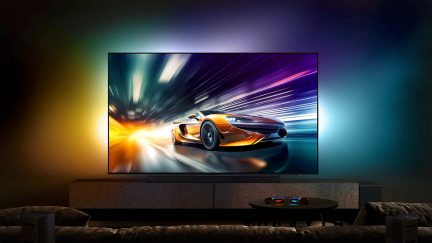 Televize v provozu zobrazující oranžové a černé sportovní auto na silnici, pohled zepředu