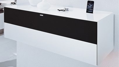 Bílý a černý nízký TV stolek, lesklá černá čelní strana, otevřená zásuvka, iPhone položený na horní desce, pohled zepředu