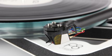 Black turntable arm with cartridge, colored cables, vinyl record in the background, close-up view