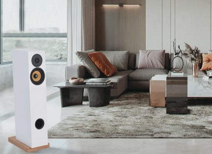 Hvid gulvhøjttaler med træfod, grå hjørnesofa med orange og grå puder, sorte og marmorerede sofaborde