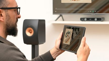 Tablette tactile contrôlant un système audio home cinéma avec enceinte hi-fi noire cuivre et TV dans salon moderne