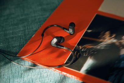 Otevřená hi-fi sluchátka Sennheiser IE 300 černá a stříbrná, intraaurální sluchátka, černý kabel, pohled shora na zeleném a oranžovém pozadí