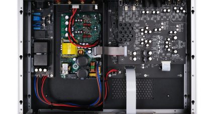 Vedere de sus a interiorului unei carcase metalice argintii și negre care conține mai multe plăci electronice verzi și negre cu condensatori cilindrici negri și albi, un transformator galben, benzi plate gri și cabluri de alimentare roșii și albastre