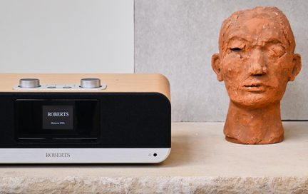Roberts Bluetune 300L Bluetooth-radio i lyst træ og sort, aluminiumsfront, placeret ved siden af en terrakottaskulpturbuste