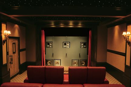 Sala cinema privata con sedili in pelle rossa, parete di altoparlanti, tende rosse, soffitto stellato, applique a muro