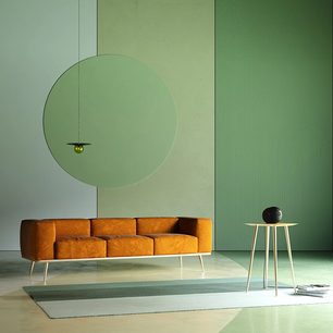 Divano arancione a 3 posti, tavolino rettangolare bianco, lampada nera con stelo bianco, disco verde appeso alla parete, pavimento grigio