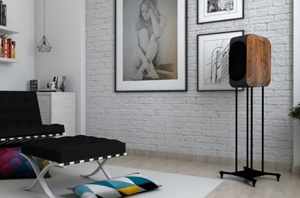 Diffusore da pavimento, vista tre quarti anteriore, cabinet in legno marrone venato tipo noce con angoli arrotondati, ampia griglia frontale ovale nera e supporto slanciato in metallo nero