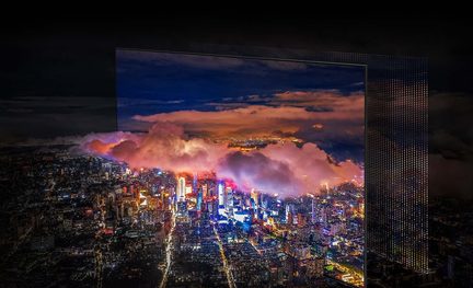 Ciudad iluminada por la noche con rascacielos y nubes rosadas, vista a través de una pantalla de televisión enmarcada en negro