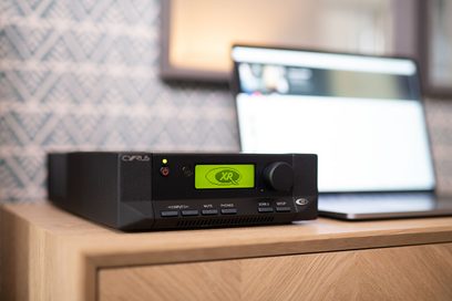 Cyrus 82 DAC QXR sort hi-fi stereforstærker, front med grøn skærm, knapper og stik, placeret på lys træhylde
