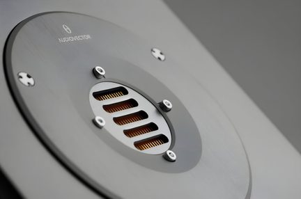 Prim-plan oblic asupra unui tweeter cu bandă, placă circulară din metal gri periat fixată cu patru șuruburi, grilaj central cu fante ce dezvăluie o bandă internă aurie