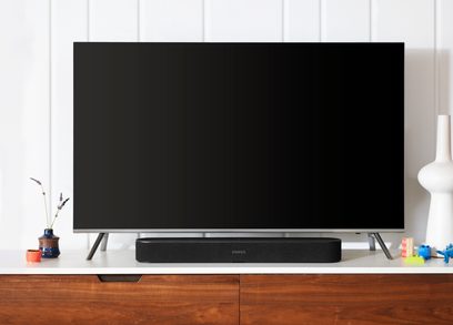 Sonos Beam sort soundbar, sort, set forfra, placeret på et træmøbel, med en slukket tv-skærm over