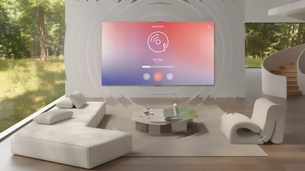Ljust minimalistiskt vardagsrum, sedd framifrån, med en stor svart väggmonterad platt-TV som visar en rosa-blå färgövergång med koncentriska ljudvågor, en låg vinklad beige tygsoffa, en skulptural ljusgrå fåtölj i skum, ett runt soffbord i kromad metall på en neutral matta och ett stort fönsterparti som vetter mot en grönskande trädgård