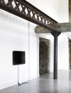 Black metal wall-mounted TV stand with decorative cross bars, mounted on a white wall near a stone archway