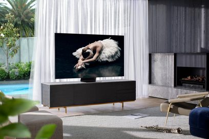 Televizor Samsung QE82Q800T zobrazující baletku ležící na černém pozadí v moderním obývacím pokoji s krbem