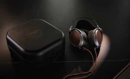Hovedtelefoner med cirkulære ørepuder, metalfinish og perforeret gitter, flettet kabel, sort rektangulært hårdt etui