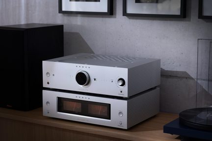 Dva stříbrné hliníkové hi‑fi přístroje v komínku, horní s velkým ovladačem, spodní s dvojitým VU měřákem, pohled ze tří čtvrtin
