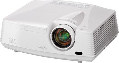 Bílý videoprojektor Mitsubishi FD630U, pohled zepředu a z úhlu, objektiv uprostřed s barevným kroužkem