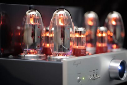 Nærbilde trekvart forfra av den integrerte stereorørforsterkeren Cayin CS-150A i sølv, sølvfarget børstet metallchassis, stort sirkulært blått bakgrunnsbelyst volumhjul og tre vippebrytere på fronten, på toppen en rad med gjennomsiktige oransje-glødende glassrør