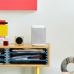 Trådløs, tilsluttet Sonos One (Gen 2) højttaler i mat hvid på træhylde med bøger og farverige dekorationsgenstande