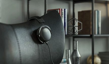 Zwarte koptelefoon opgehangen aan een rugleuning van een zwarte leren stoel, metalen plank met boeken en decoratieve objecten op de achtergrond.
