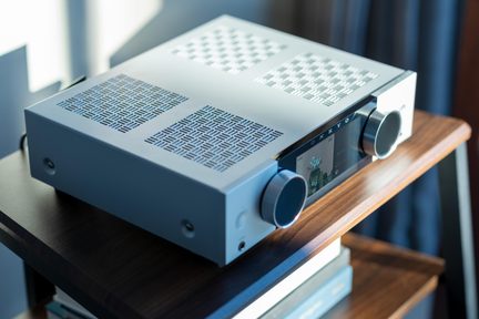 Sølvfarvet Onkyo hi-fi-forstærker med farvedisplay på fronten og to store drejeknapper, placeret på en træhylde